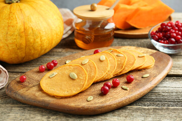 Tasty pumpkin pancakes with seeds, cranberries and honey on wooden table, closeup