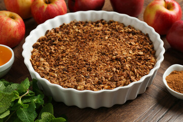 Tasty apple crisp in baking dish and ingredients on wooden table, closeup
