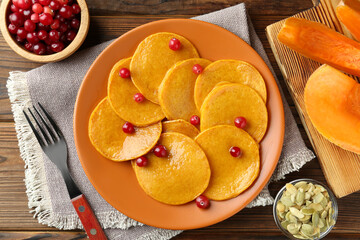 Tasty pumpkin pancakes with cranberries served on wooden table, flat lay