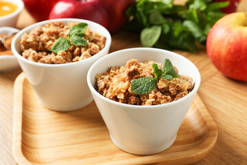 Delicious apple crisp with mint in bowls on wooden table, closeup