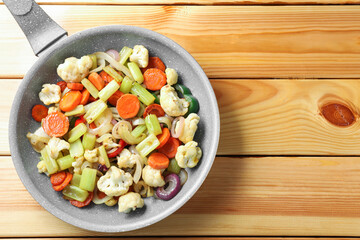 Frying pan with vegetables on wooden table, top view. Space for text