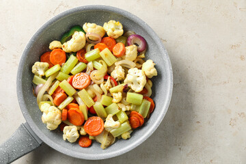 Frying pan with vegetables on light textured table, top view. Space for text
