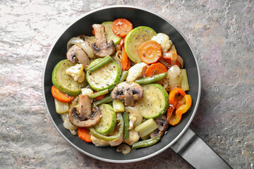 Different vegetables and mushrooms in frying pan on grey textured table, top view
