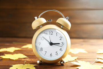 Autumn time. Alarm clock and golden leaves on wooden table