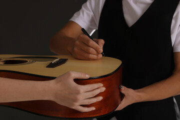 Musician signing autograph on guitar against black background, closeup