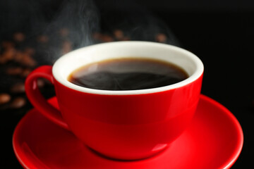 Red cup with coffee and roasted beans on black background, closeup