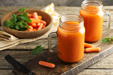 Fresh carrot juice in mason jars, vegetables and mint on wooden table