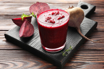 Fresh beetroot smoothie in glass and cut vegetable on wooden table, closeup