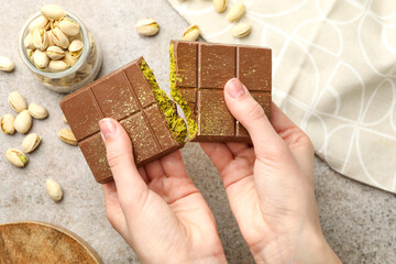 Woman breaking Dubai chocolate bar with pistachios and knafeh at grey table, closeup