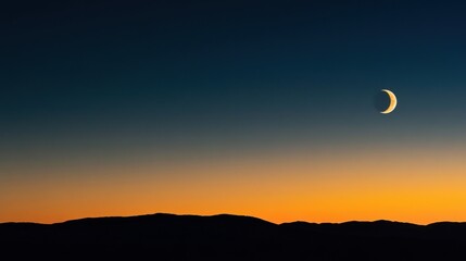 Obraz premium A crescent moon in a clear twilight sky over silhouetted mountains with a gradient of blue to orange