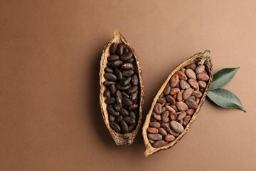 Cocoa pods with beans and leaves on brown background, flat lay. Space for text