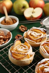 Tasty apple roses with powdered sugar served on green wooden table, closeup