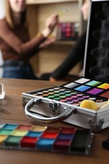 Face paints on wooden table and artist working with client indoors, selective focus