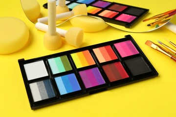 Face paints and tools on yellow background, closeup