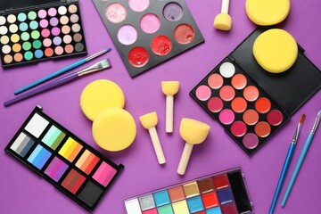 Face paints, tools and makeup products on purple background, flat lay
