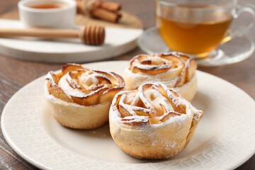 Freshly baked apple roses, honey and tea on table, closeup