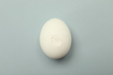 One egg with cracked shell on grey background, top view