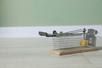 Metal mouse trap with piece of cheese indoors, space for text