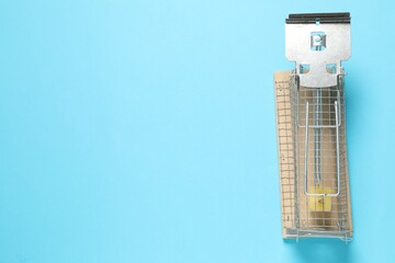 Metal mouse trap with piece of cheese on light blue background, top view. Space for text