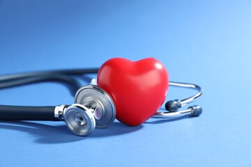 Stethoscope and red decorative heart on blue background, closeup