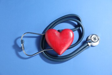 Stethoscope and red decorative heart on blue background, top view