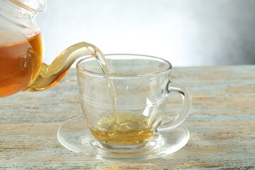 Pouring freshly brewed tea from teapot into glass cup on wooden table, closeup