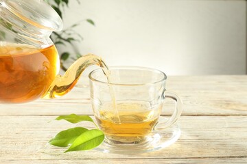Pouring freshly brewed tea from teapot into glass cup on wooden table, closeup