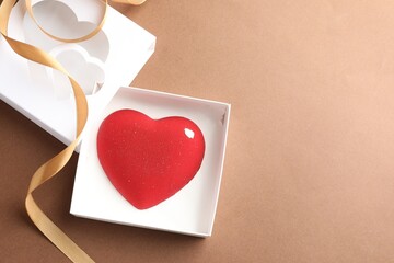 Heart shaped chocolate in box on brown background, top view. Space for text