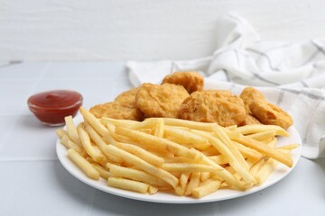 Tasty chicken nuggets and french fries with sauce on white tiled table, closeup