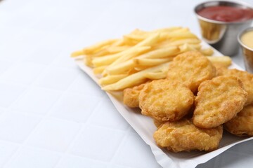 Tasty chicken nuggets and french fries with sauce on white tiled table, closeup. Space for text