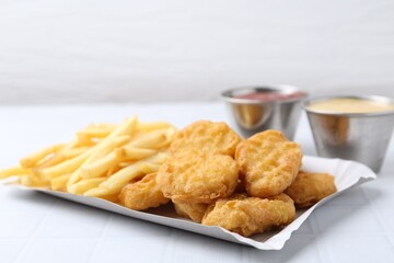 Tasty chicken nuggets and french fries with sauce on white tiled table, closeup. Space for text