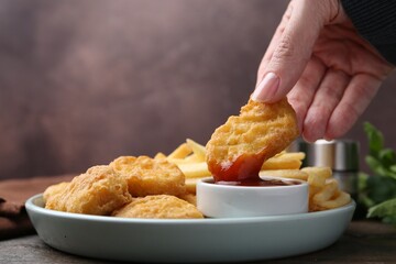 Woman eating tasty chicken nuggets and french fries with sauce at wooden table, closeup. Space for text