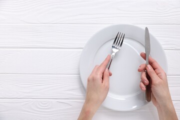 Woman with cutlery and empty plate at white wooden table, top view. Space for text