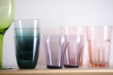 Empty clean glasses on wooden shelf near white wall indoors, closeup