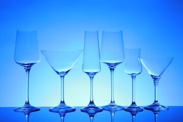 Many empty clean glasses on mirror surface against blue background