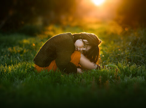 Child in sunset glow, nestled on lush green grass with orange trees