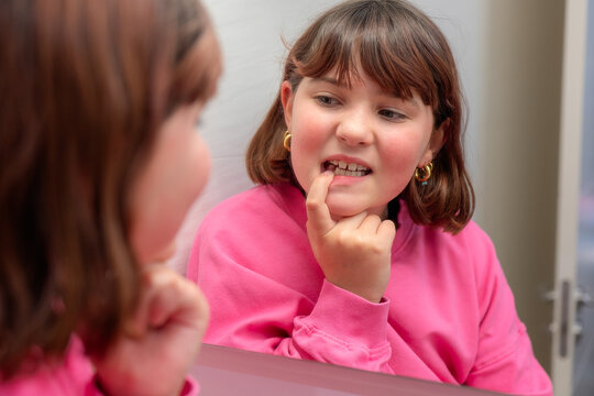Young girl examining her loose milk tooth in the mirror