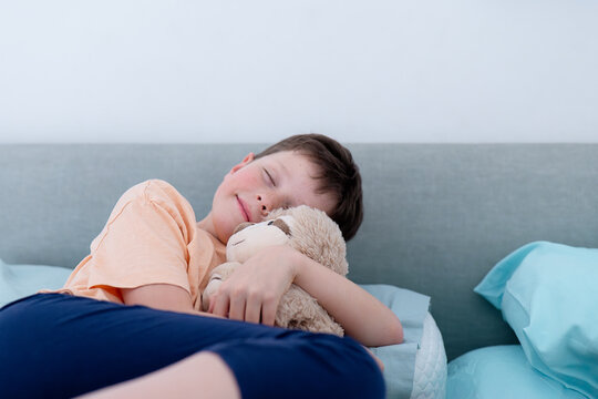Young boy napping with his teddy bear on a couch