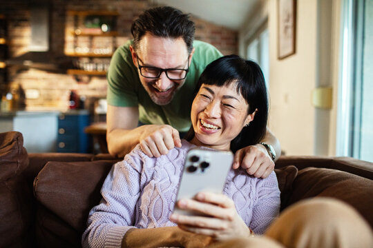 Happy couple laughing while looking at smartphone at home