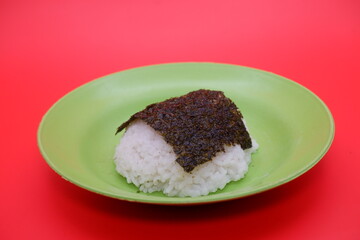 Rice Topped with Dried Nori Seaweed on a Green Plate, Isolated on Red Background