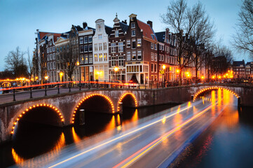 Traditional houses on Amsterdam canal during blue hours. Night view with light trail of passing boat