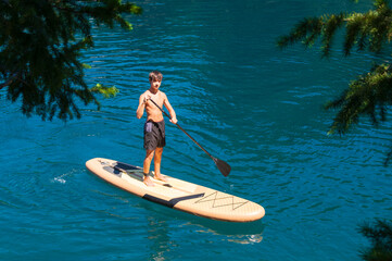 Teenage boy enjoying his stand up paddle board on mountain lakes during his summer vacation.