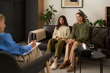 Full length portrait of concerned mother with teenage girl talking to female therapist during...