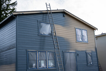 New home professional painting project in process, back of two-story house exterior with aluminum...
