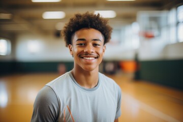 Fototapeta premium Smiling portrait of a young male African American basketball player wearing a white t shirt in an indoor basketball gym