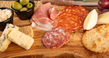 A wooden board with a variety of food items including crackers, cheese, olives, and meat