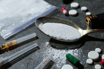 Drug addiction. Plastic bag with powder, spoon, and syringes on gray textured table, closeup