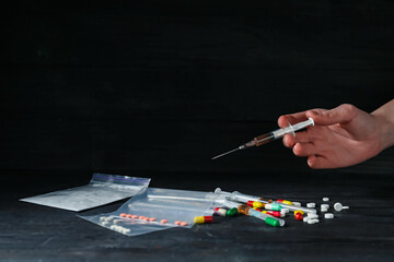 Drug addiction. Woman with syringe at black wooden table against dark background, closeup. Space...