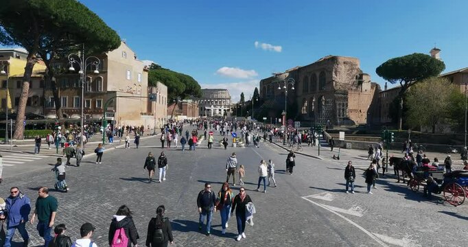 Timelapse of crowd of tourists people exploring Via dei Fori Imperiali street toward Colosseum on a sunny eastern day in Rome when the street is forbidden for traffic and is made a walkway