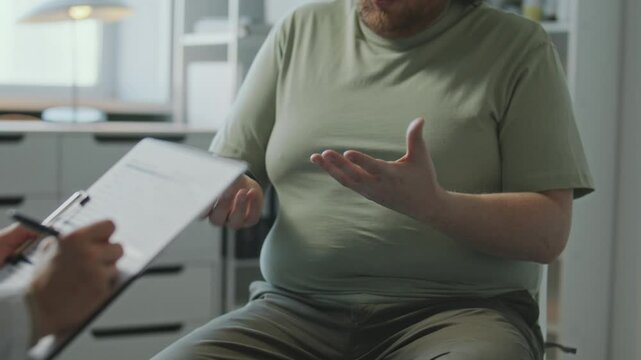 Overweight patient touching his stomach and consulting doctor about weight loss during visit to clinic. Midsection shot